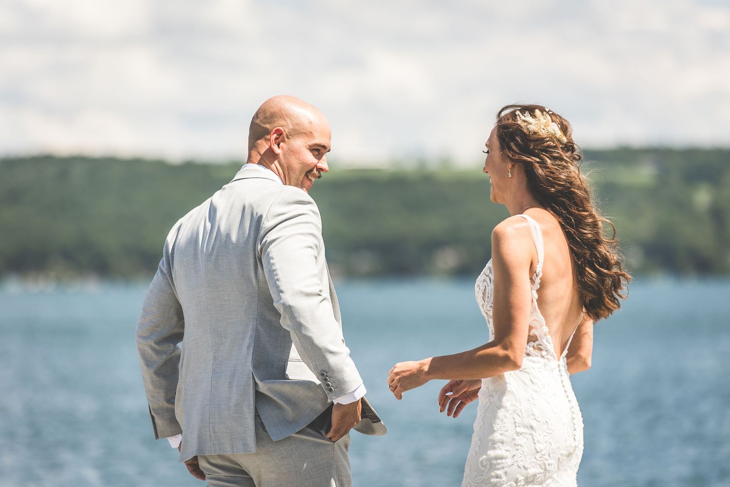 A couple in wedding attire shares a candid moment on their special day by a scenic lake.