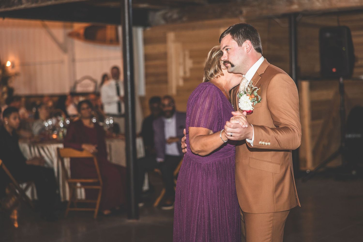 Wedding guests dancing in pairs at rustic barn reception with string lights.