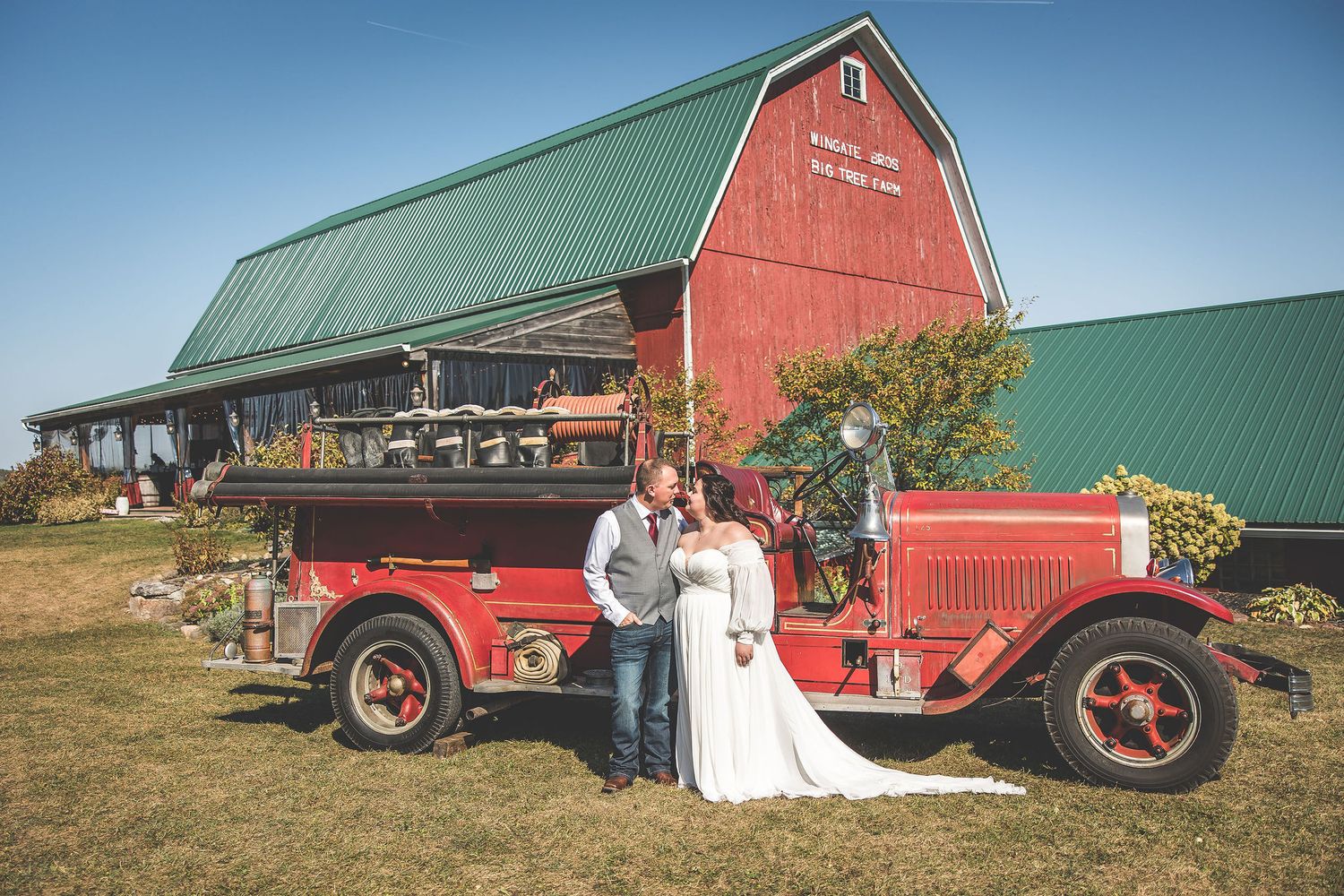 Vintage red fire truck parked near rustic barn creates unique wedding photo backdrop.
