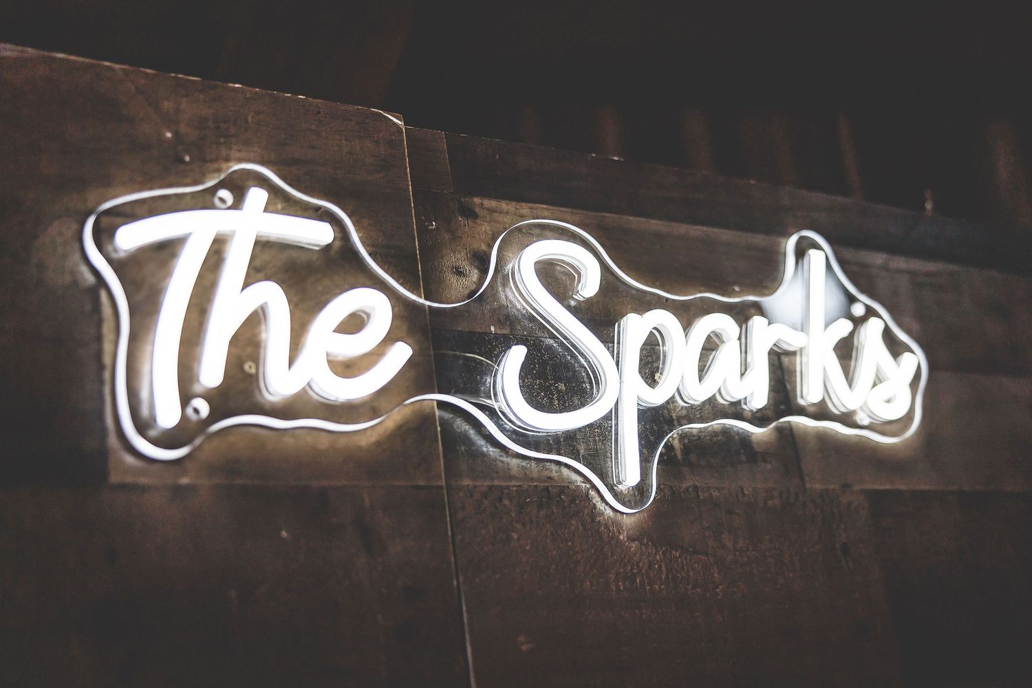 Illuminated neon sign spelling 'The Spark' mounted on dark wooden wall.