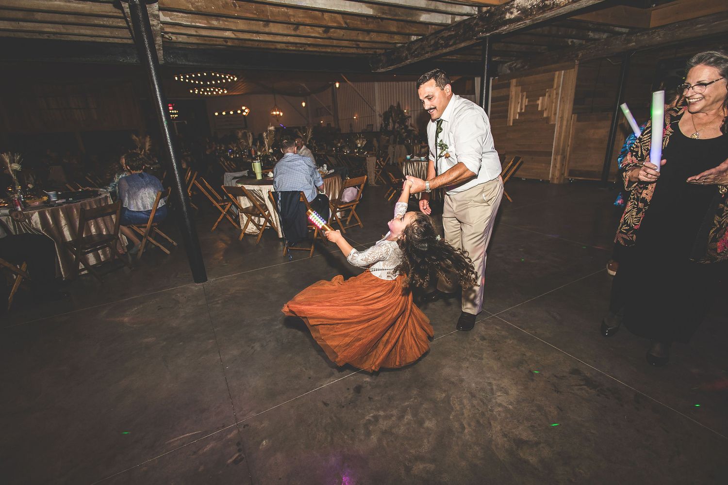 Wedding guests dancing energetically on rustic barn dance floor during reception celebration.