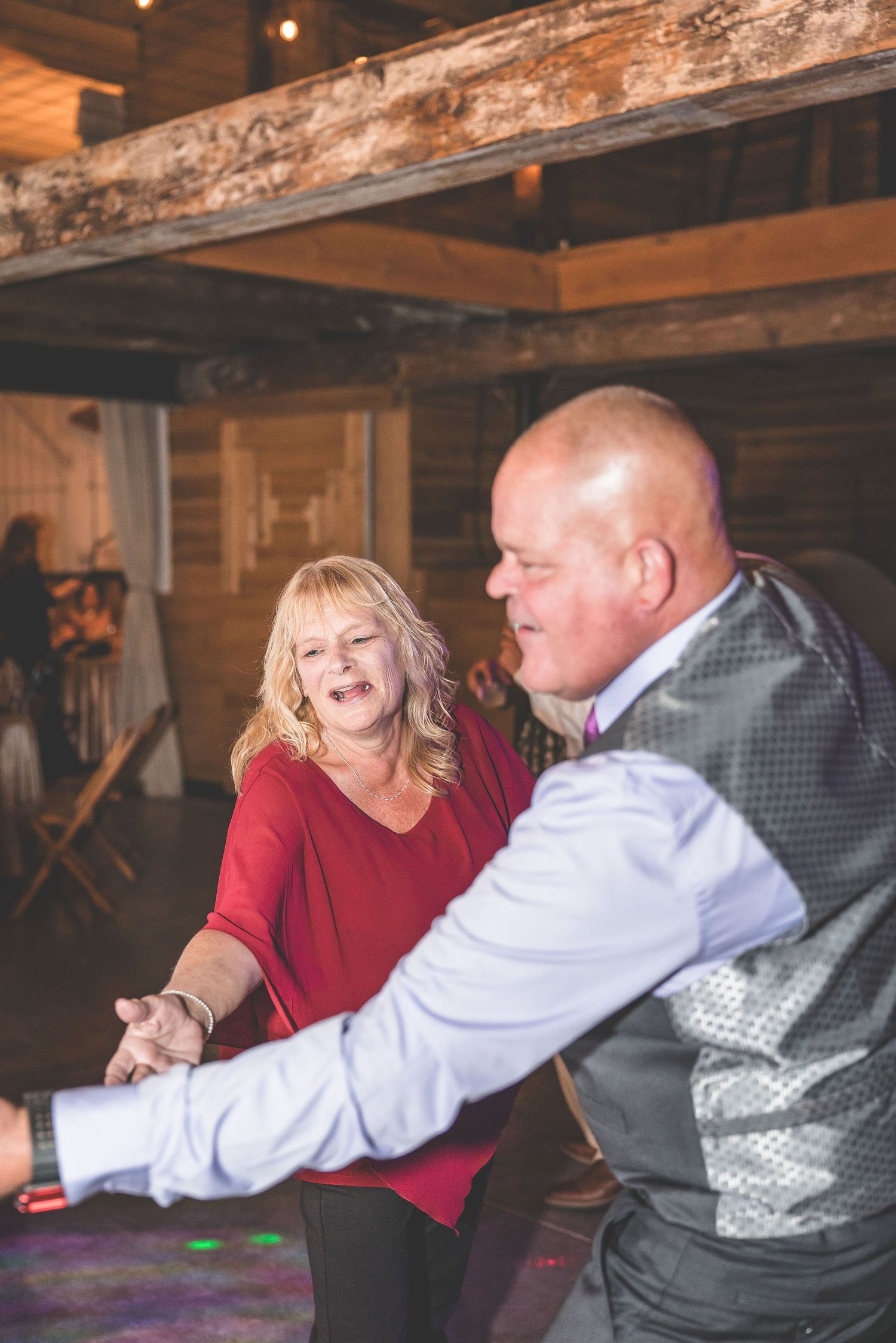 Guests share laughter while dancing together in a rustic barn-style venue with exposed wooden beams.