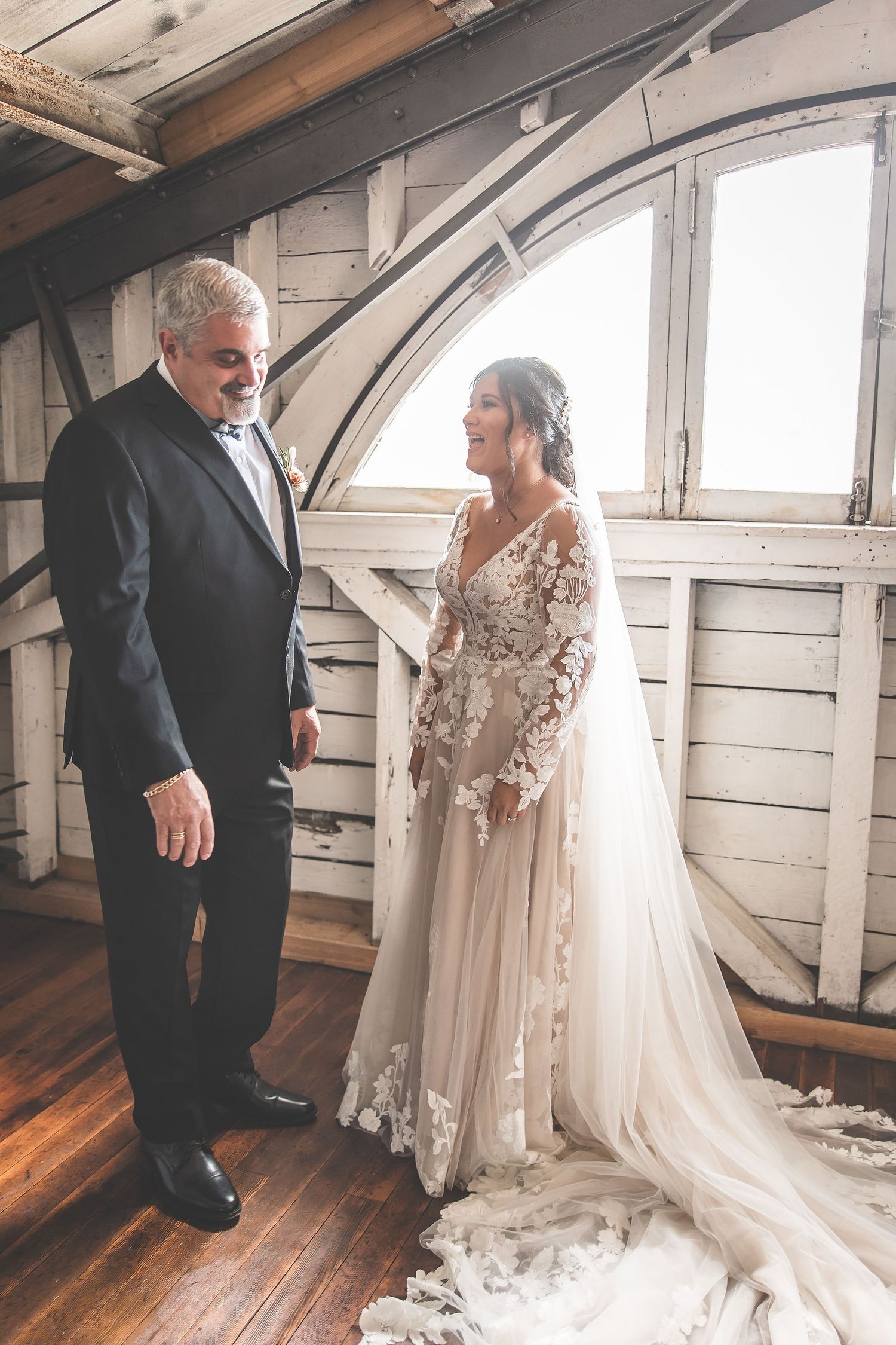 A wedding scene unfolds in a rustic attic space with white walls and wooden floors.