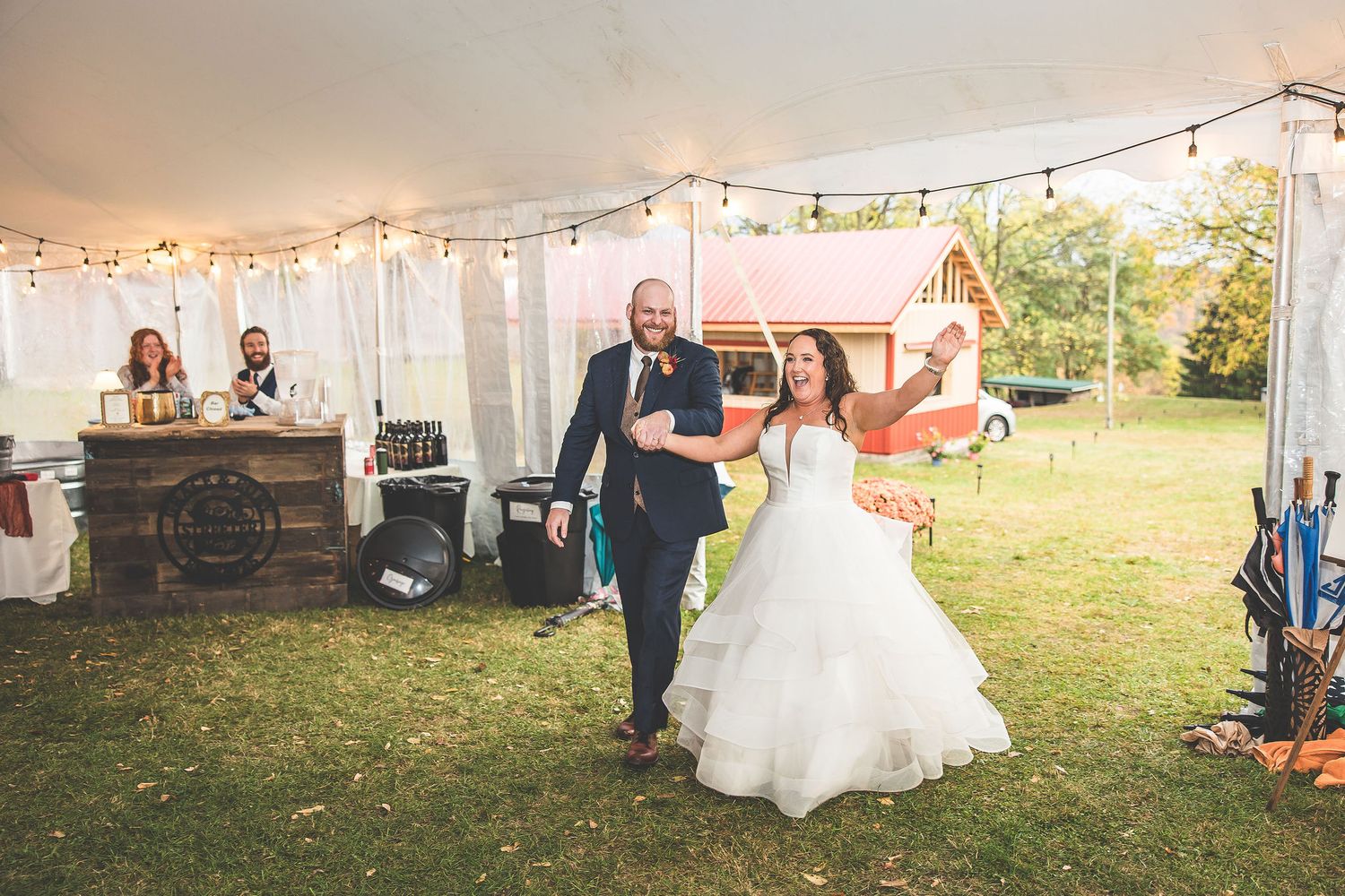 Evening wedding reception under white tent with string lights and outdoor scenery visible.