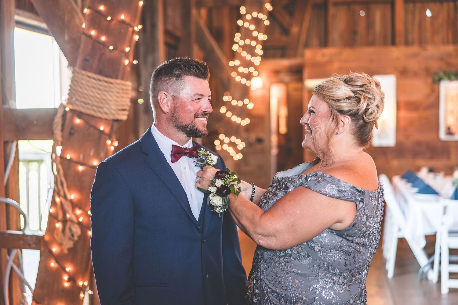 Rustic barn wedding reception venue decorated with twinkling lights and pink fabric draping from wooden beams.