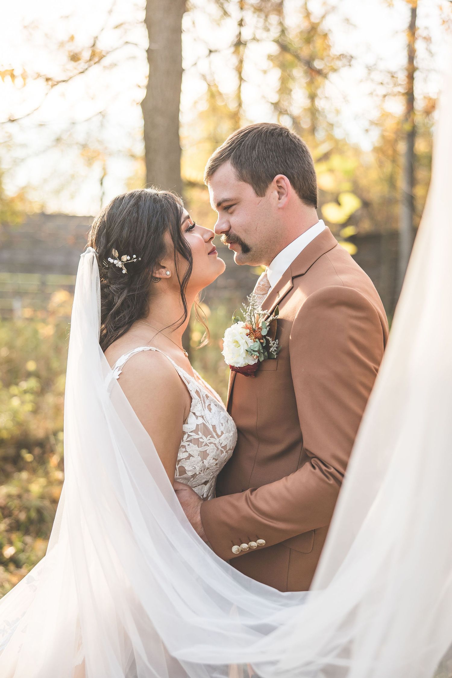 Flowing white veil creates dramatic frame around couple during autumn wedding photoshoot.