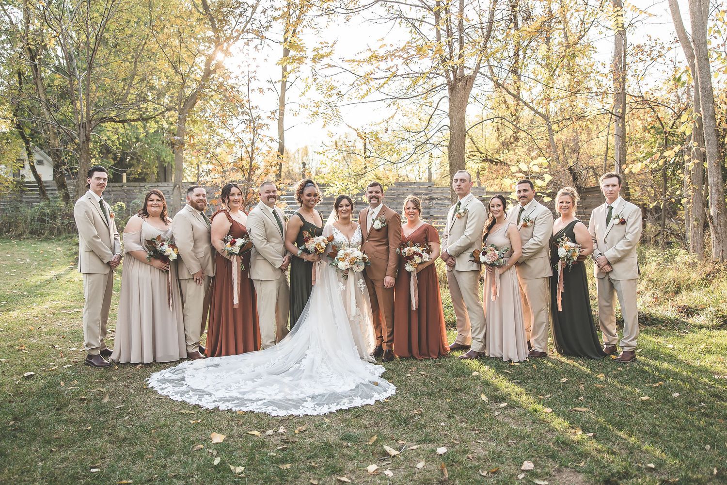 Wedding party arranged in outdoor setting with neutral color palette and dramatic train on wedding dress.