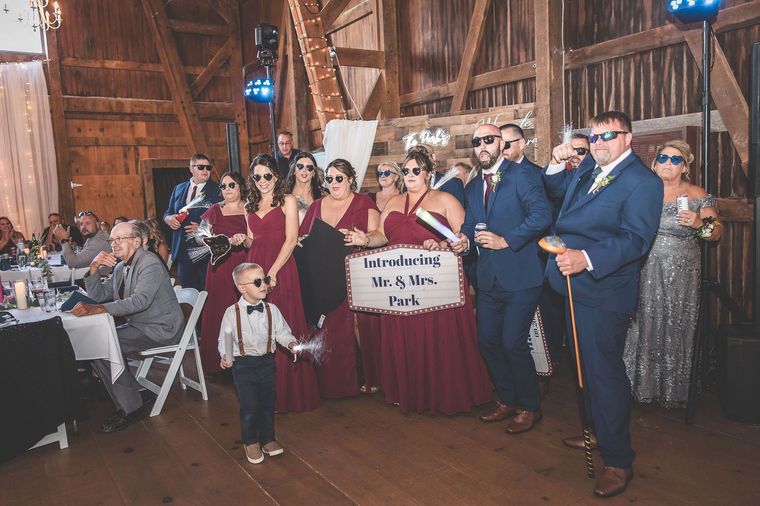 Large group of wedding guests gathered on dance floor of rustic barn venue during reception celebration.