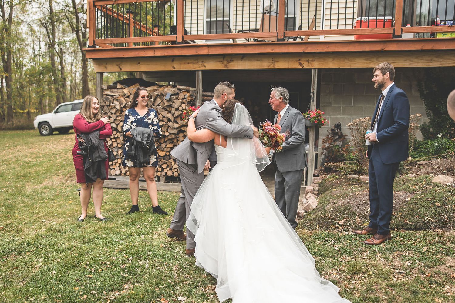 Outdoor autumn wedding celebration with rustic wooden deck in background.