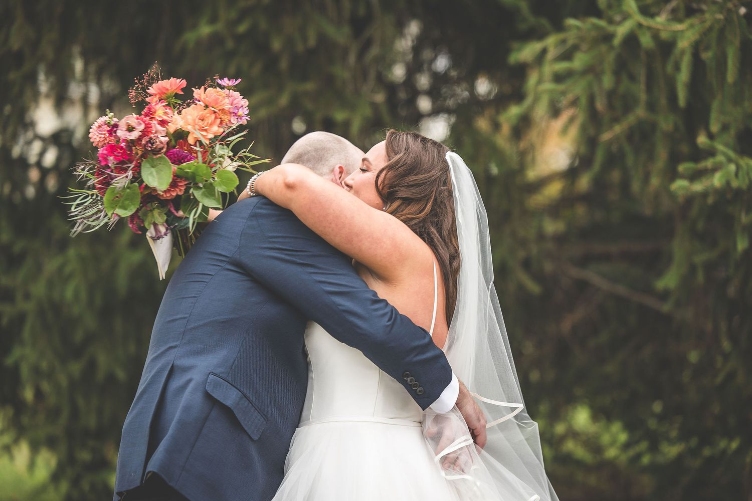 A couple embraces during their wedding ceremony with a colorful bouquet in hand.