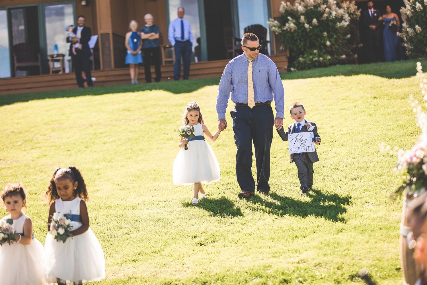 Wedding party walking across sunny lawn with flower baskets and decorations.
