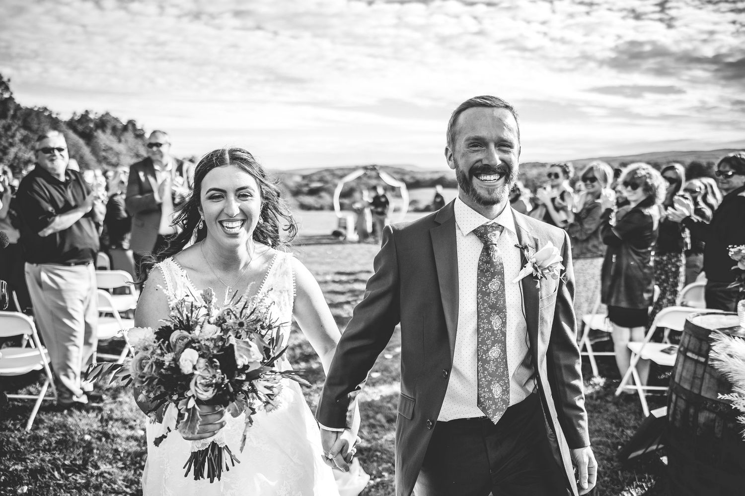 Black and white panorama captures joyful moments during outdoor wedding celebration.