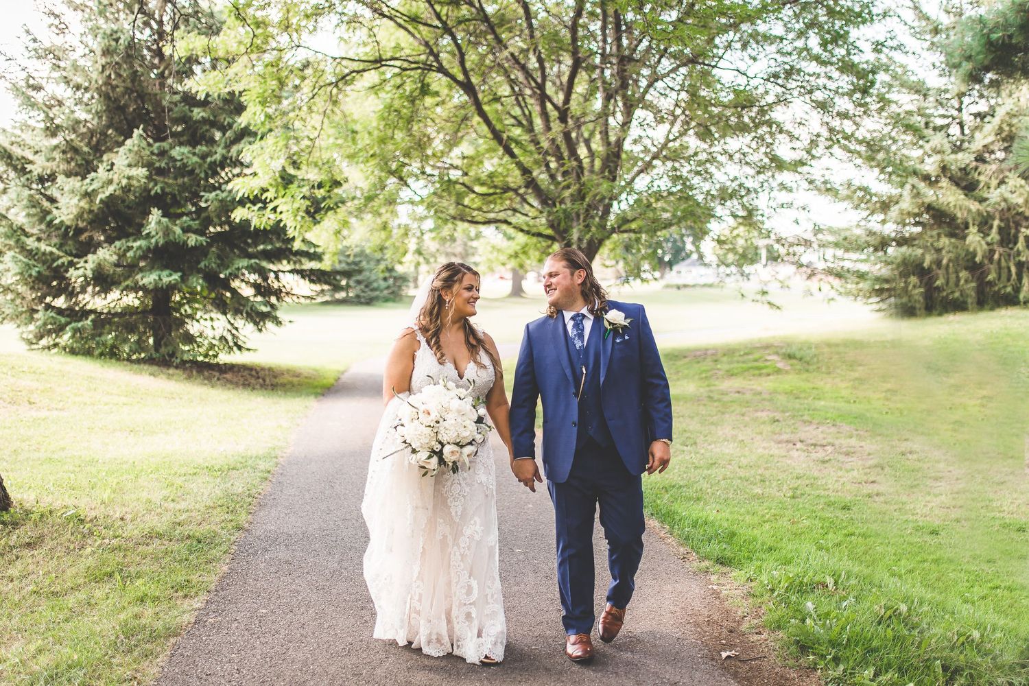 Couple walks hand in hand along a garden path surrounded by green trees.