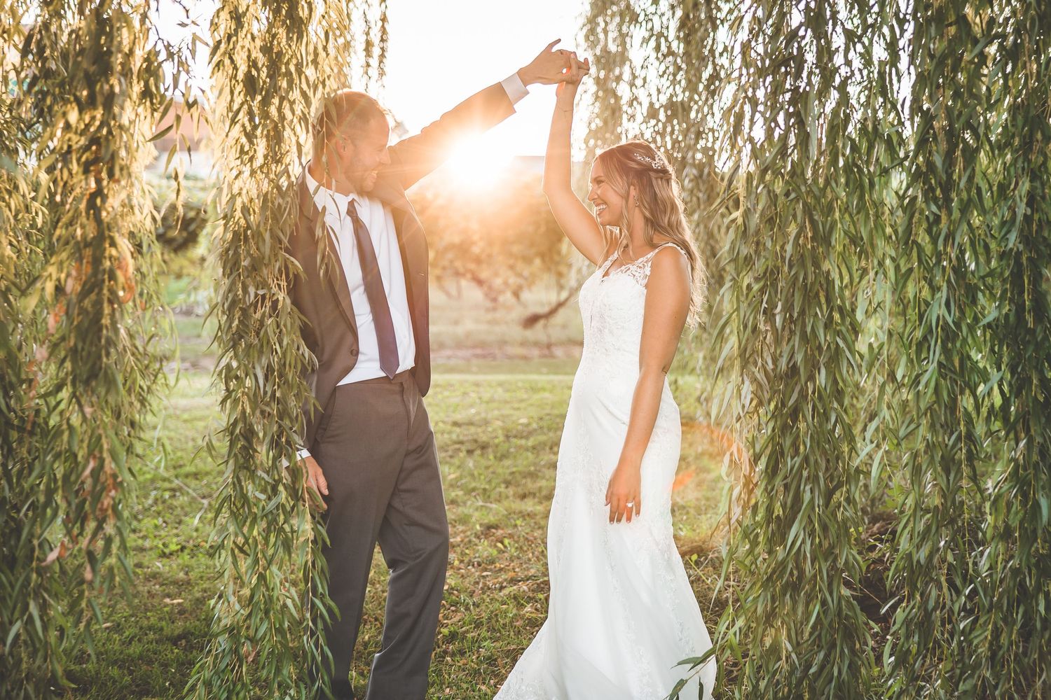 Golden sunlight filters through willow branches as newlyweds share an intimate moment.