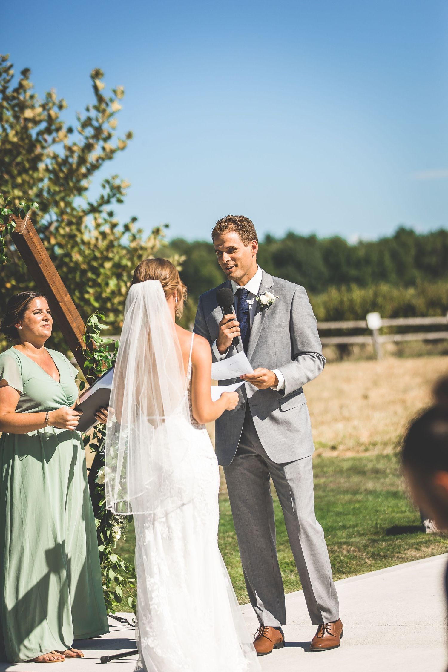 Outdoor wedding ceremony with bridesmaids in mint green dresses and guests seated on white chairs.
