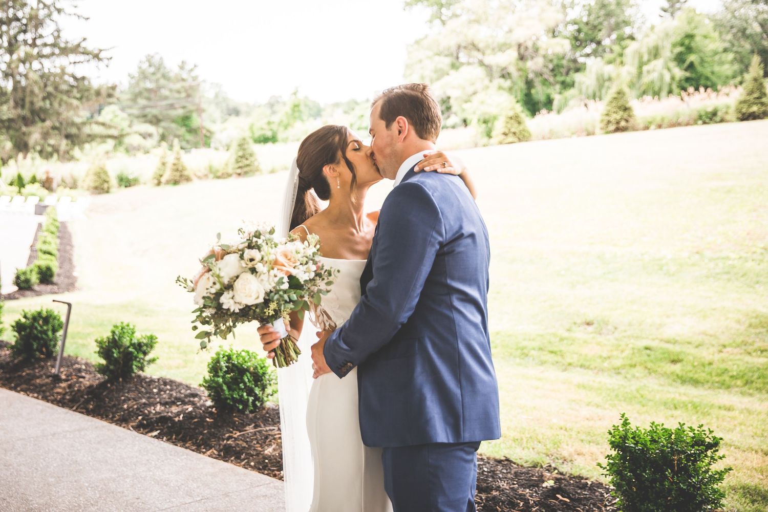 Couple shares intimate first look moment in landscaped garden setting.