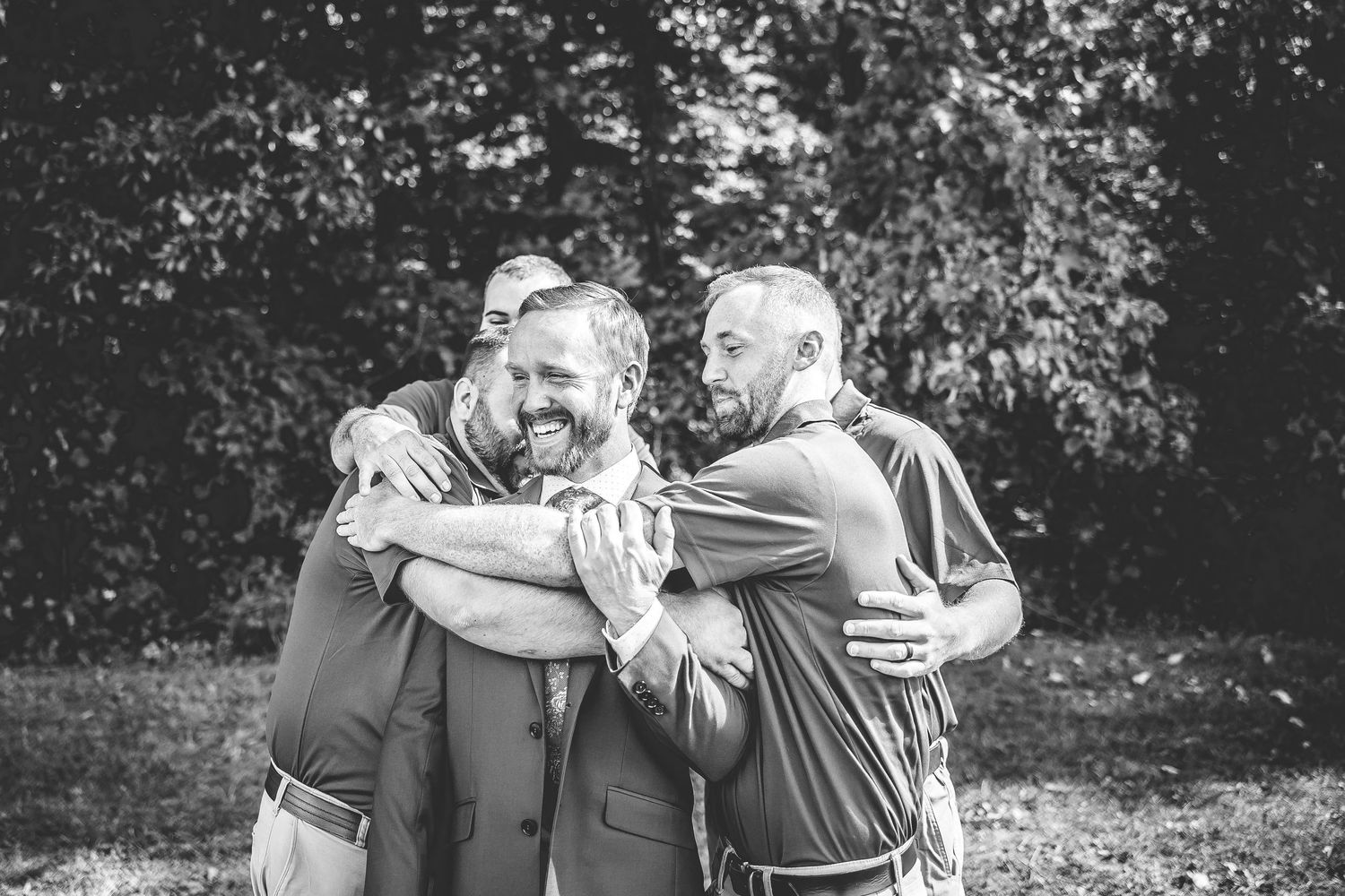 Wedding party members embrace in casual group photo outdoors.
