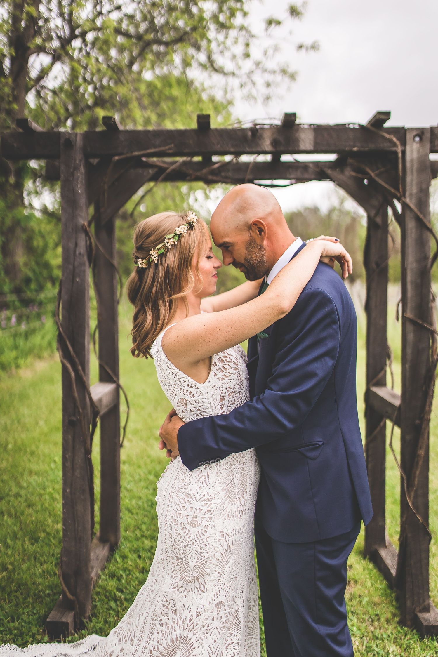 A tender moment between newlyweds beneath a wooden arch surrounded by spring greenery.