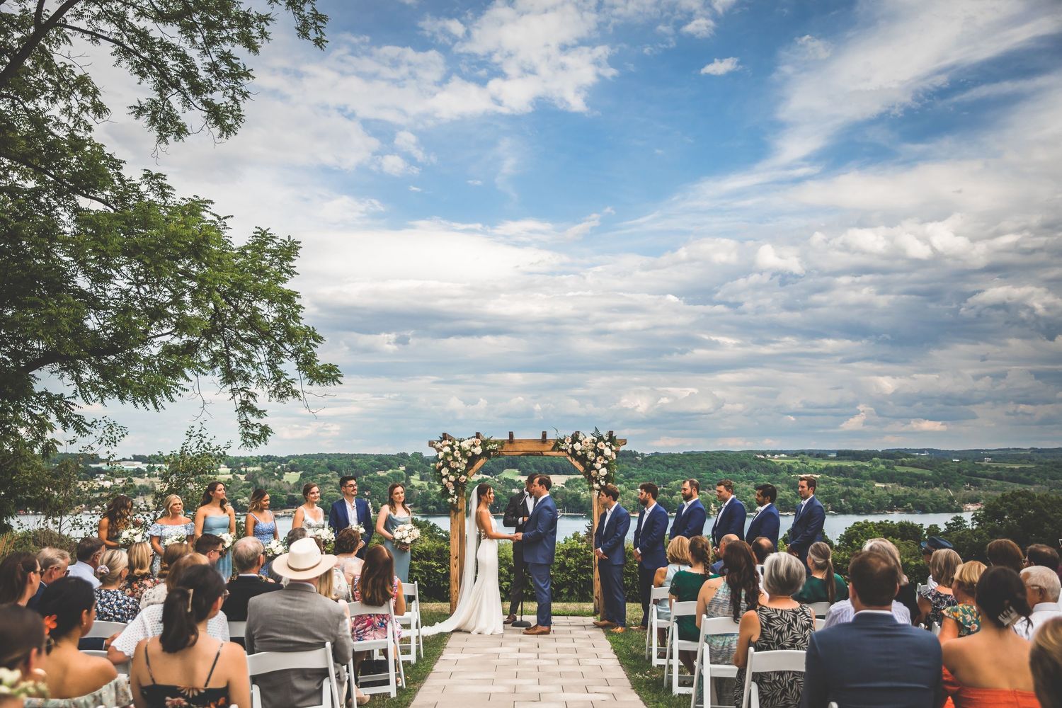 Wide angle shot of wedding guests seated at an outdoor hilltop venue with scenic mountain views.