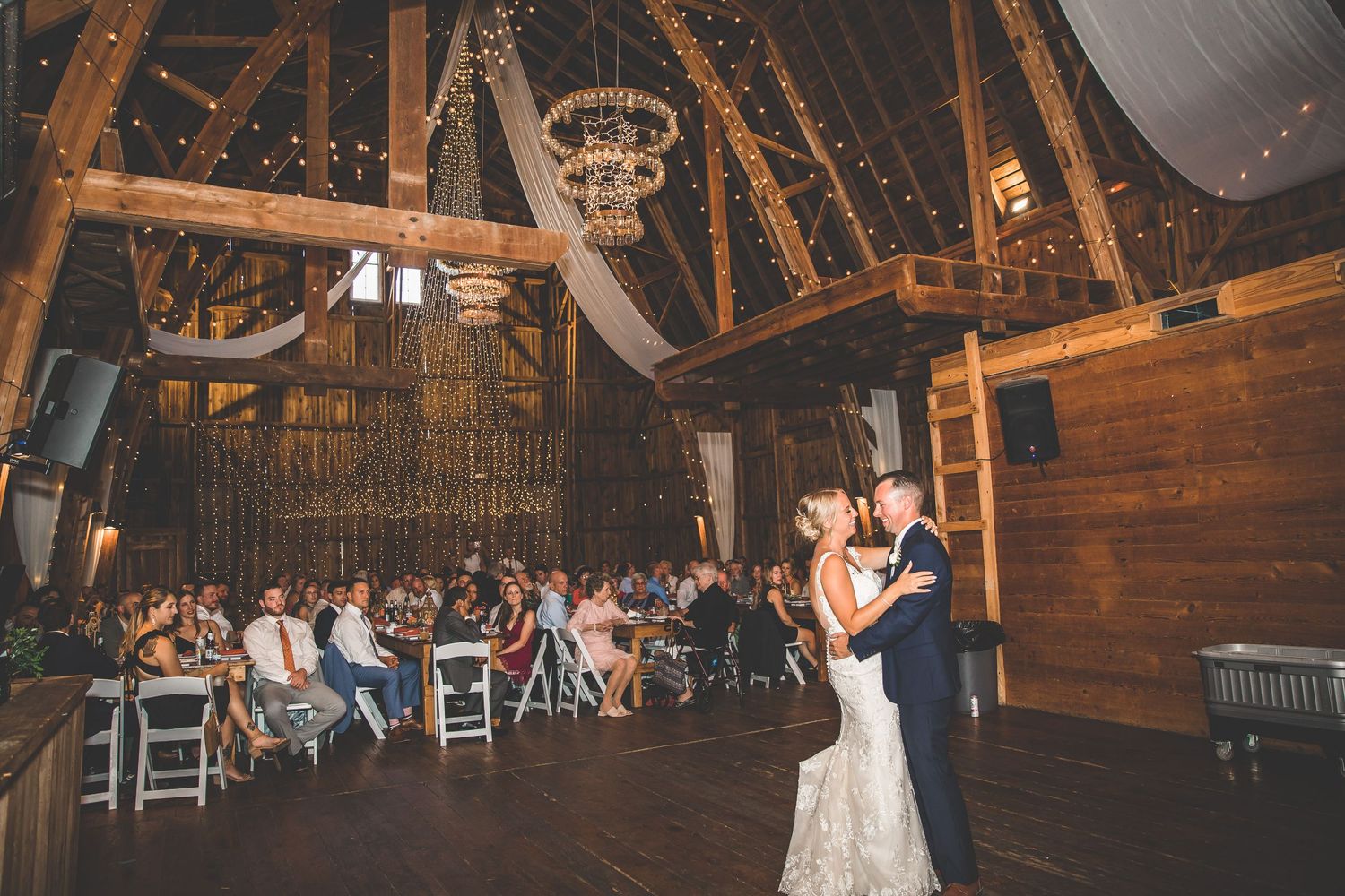 Wide angle view of a rustic barn wedding venue with wooden beams and elegant decor.