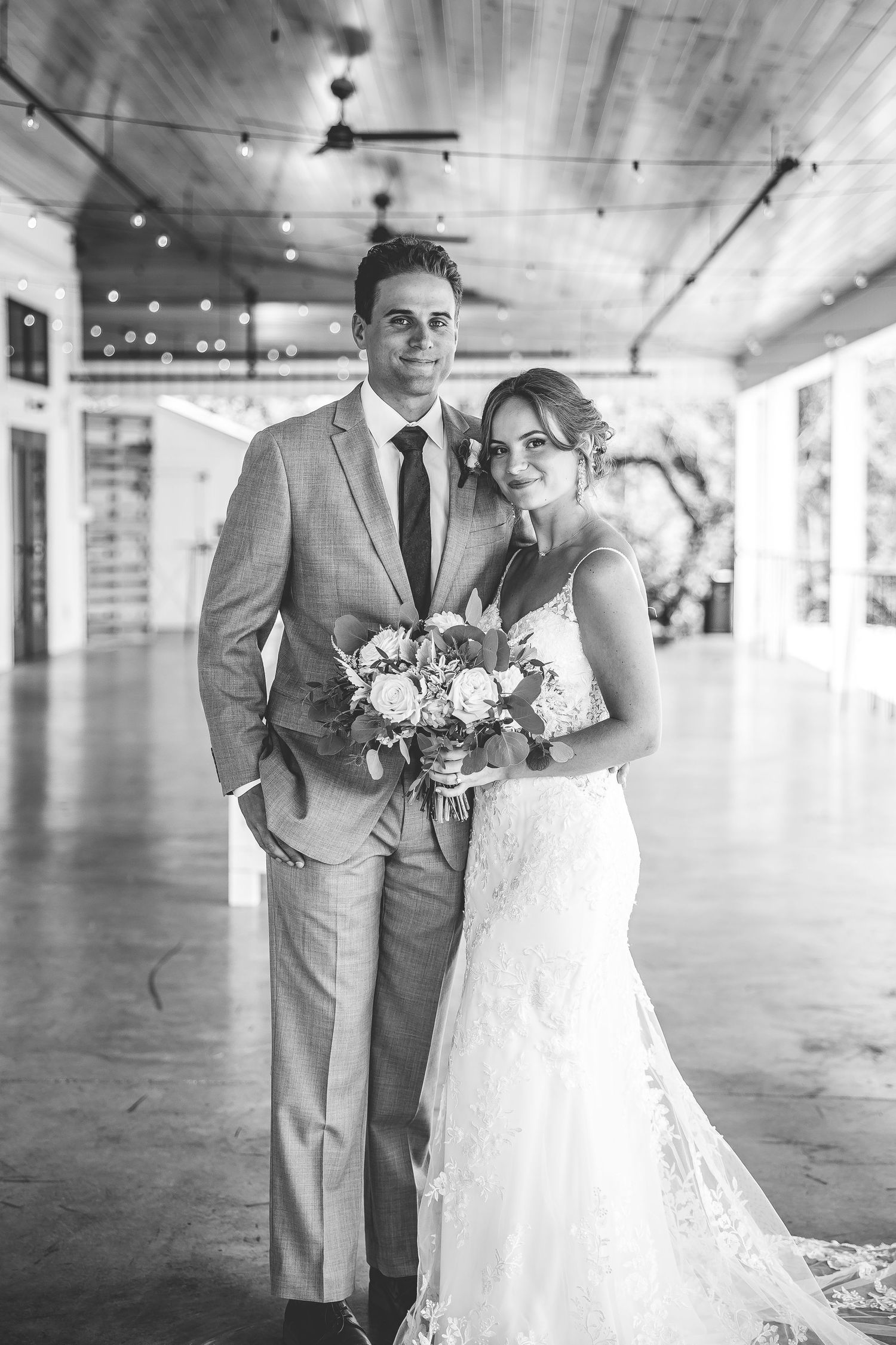 Black and white wedding portrait under a covered porch with elegant lighting.