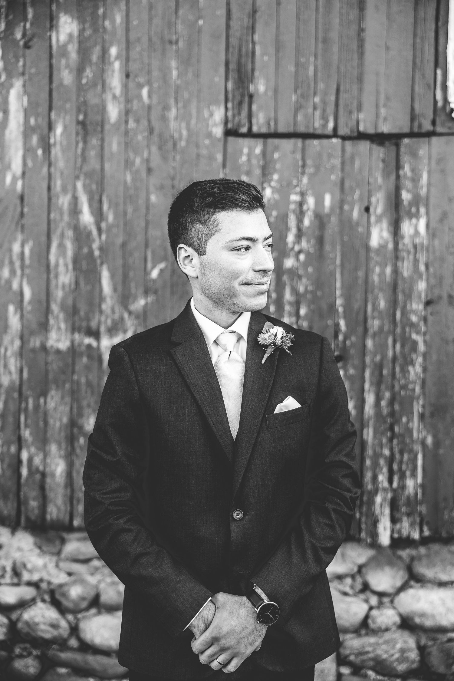 Black and white portraits of groom in formal attire against weathered barn siding.