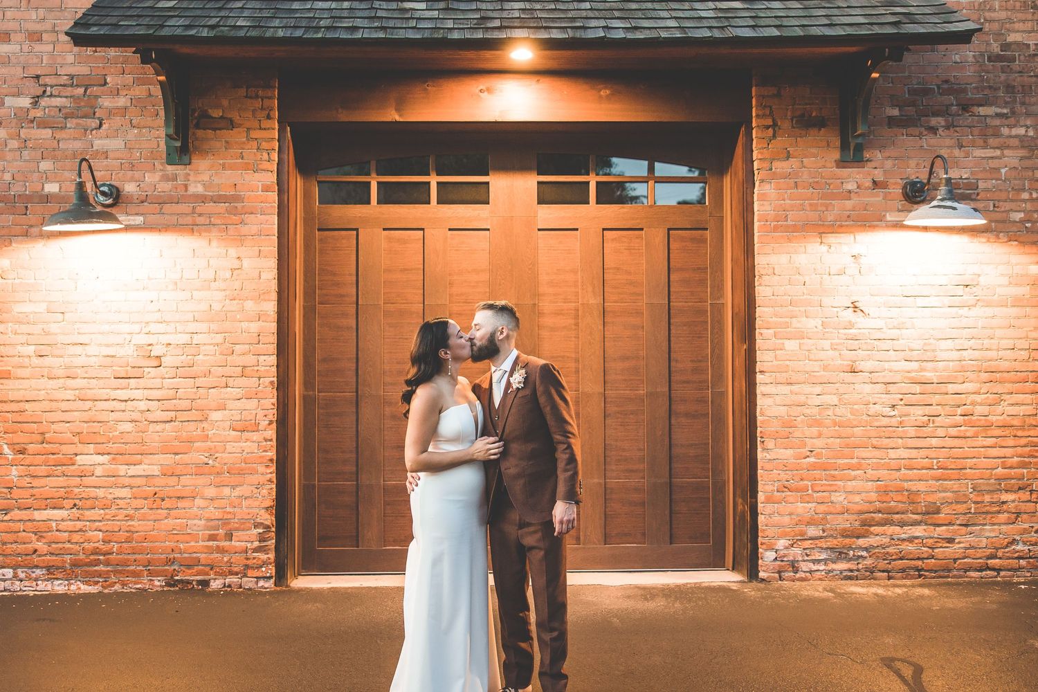 Romantic nighttime portrait in front of wooden doors with brick wall and warm lighting.