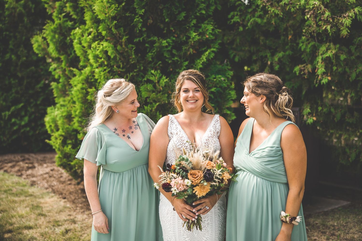 Bridesmaids in mint green dresses pose together with bouquets against a natural backdrop.