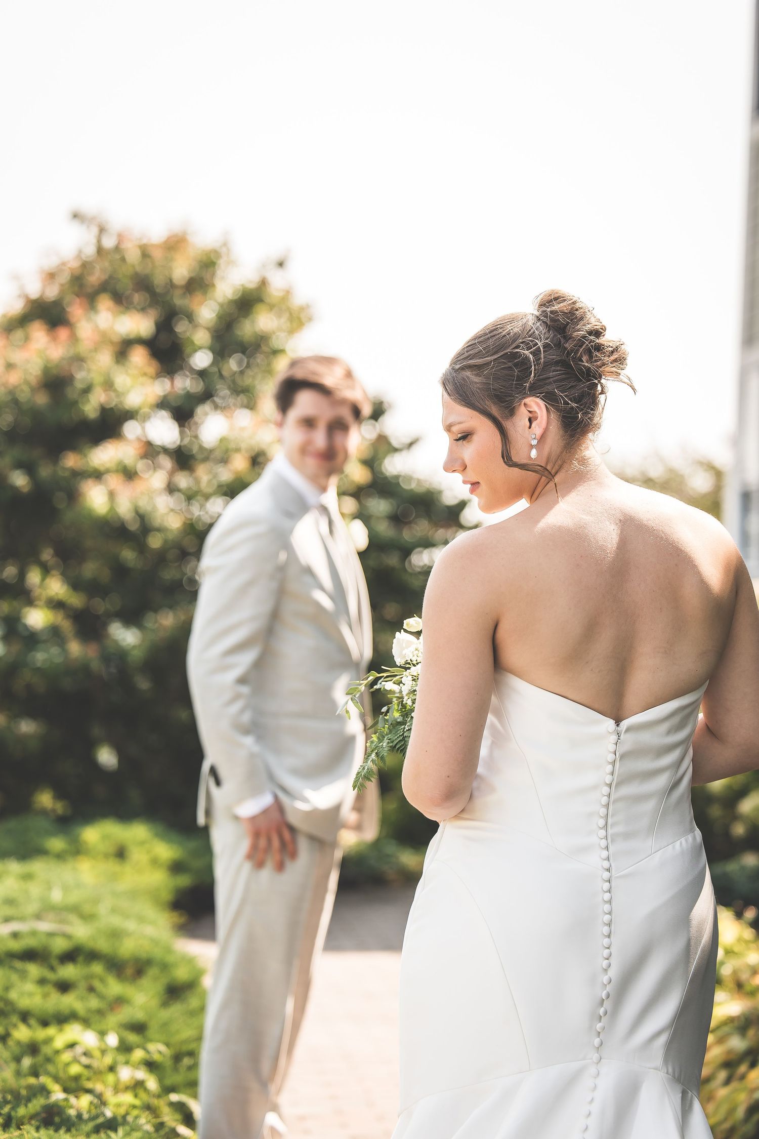 Wedding couple poses in soft sunlight with focus on bride's elegant dress details.