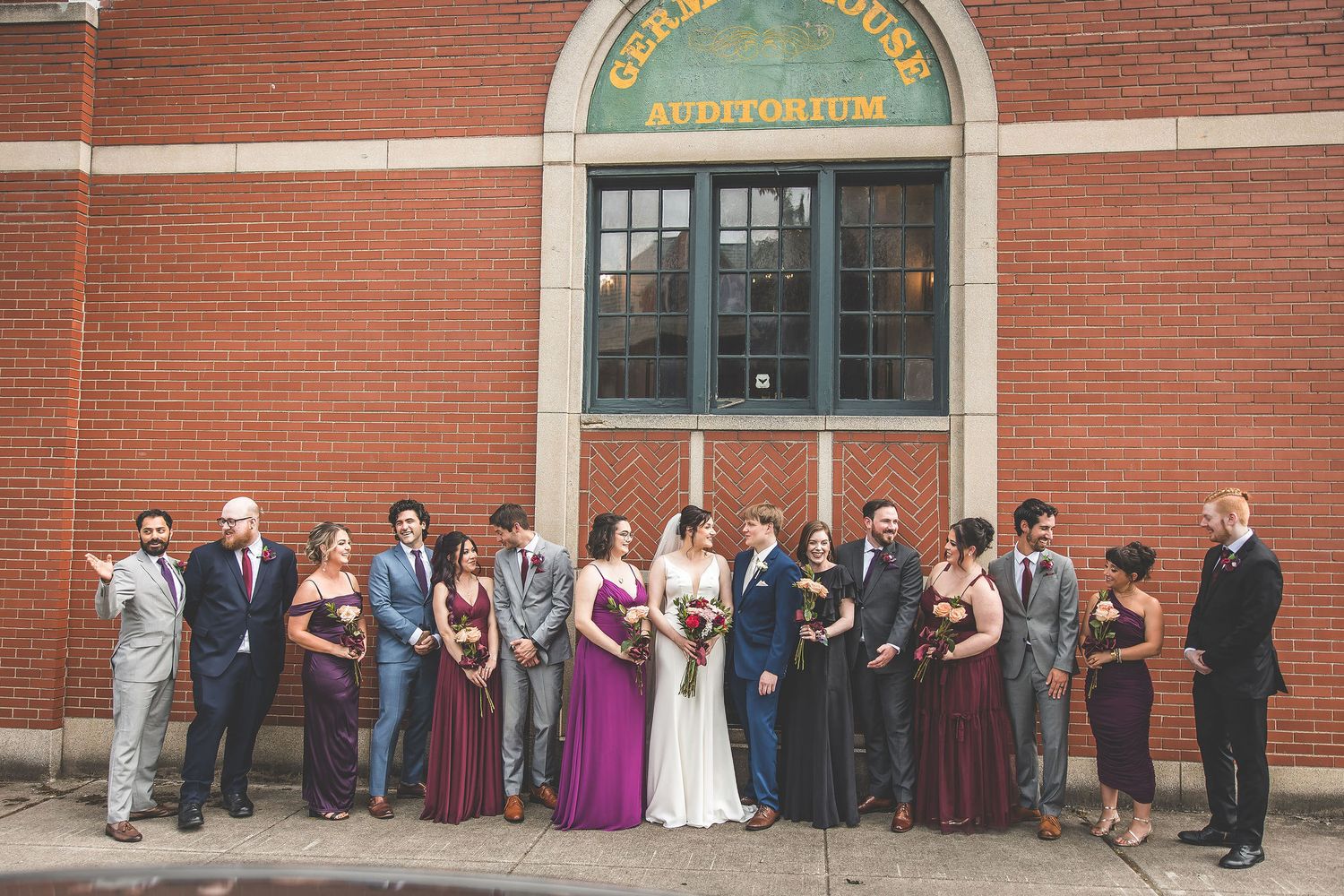 Wedding party poses in front of a historic red brick building with an auditorium entrance.