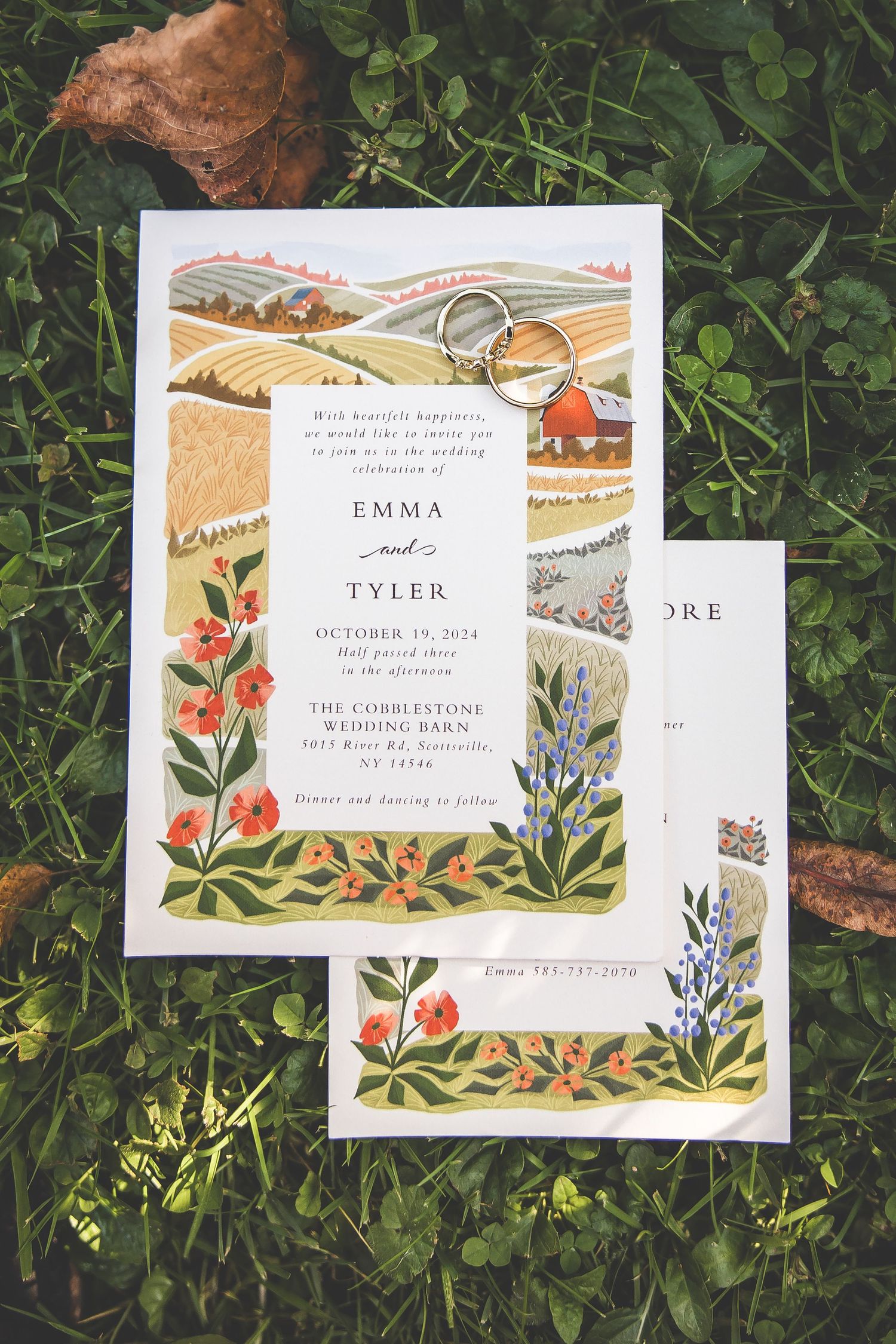 Floral wedding invitation with watercolor landscape design laying on green foliage.