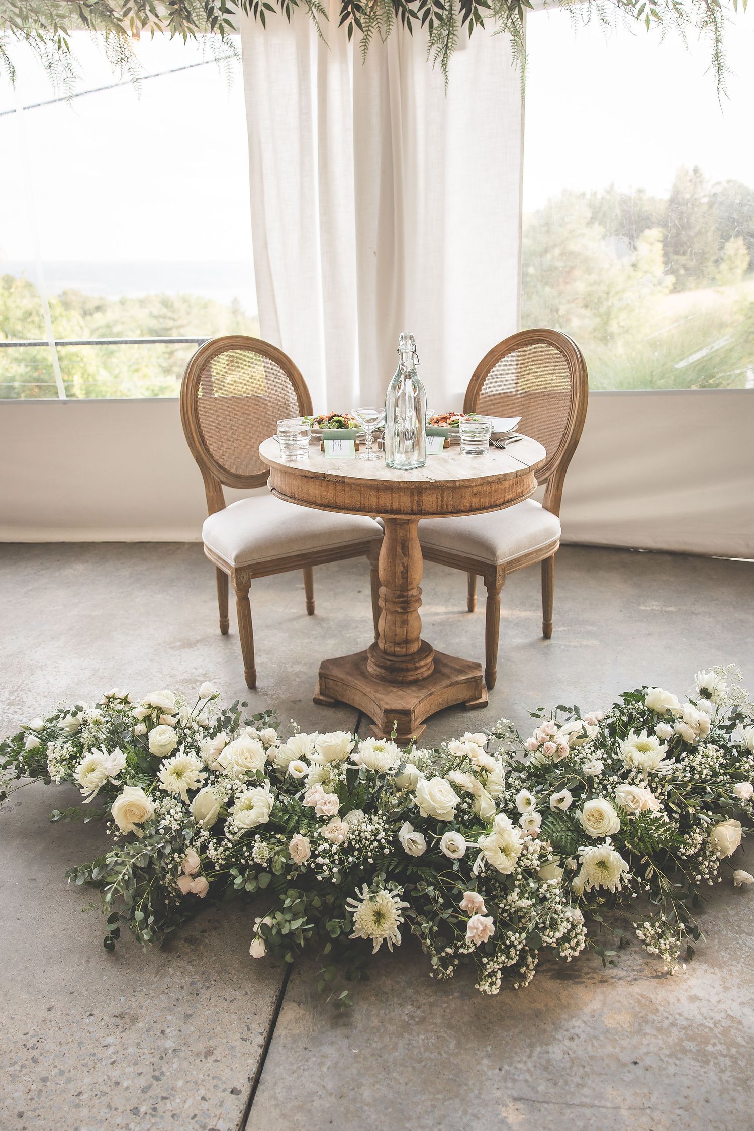 Elegant seating area with round wooden tables adorned with lush white floral arrangements.