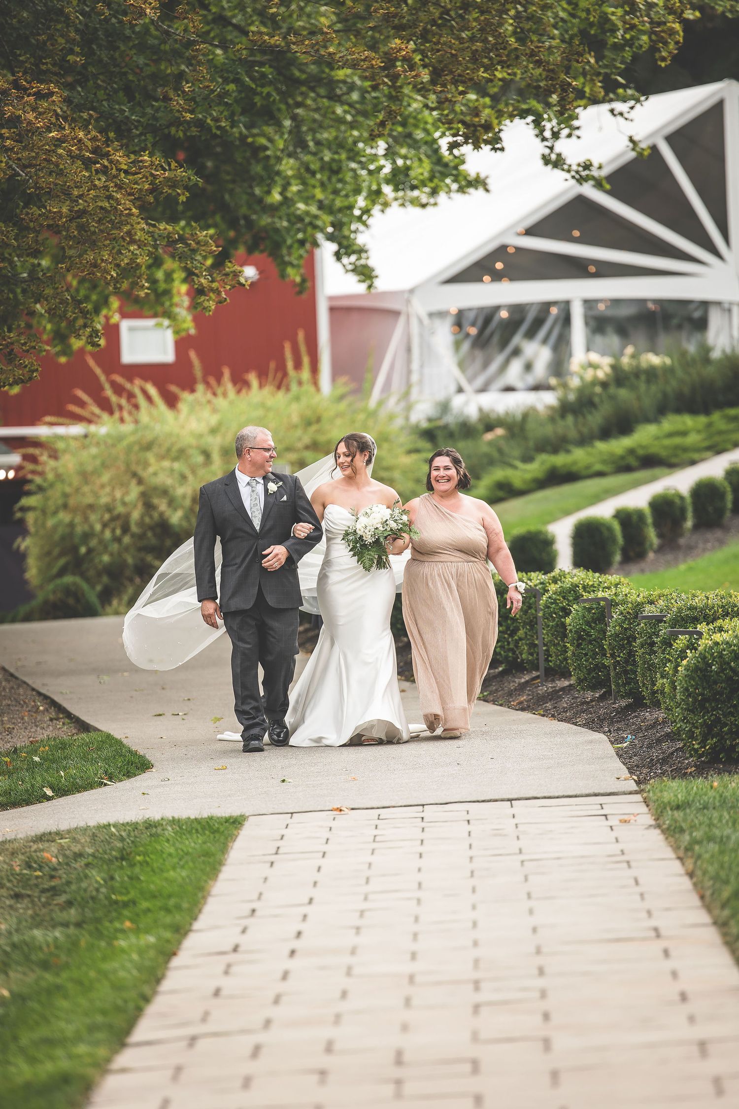Wedding party members walk along stone pathway surrounded by landscaped gardens.