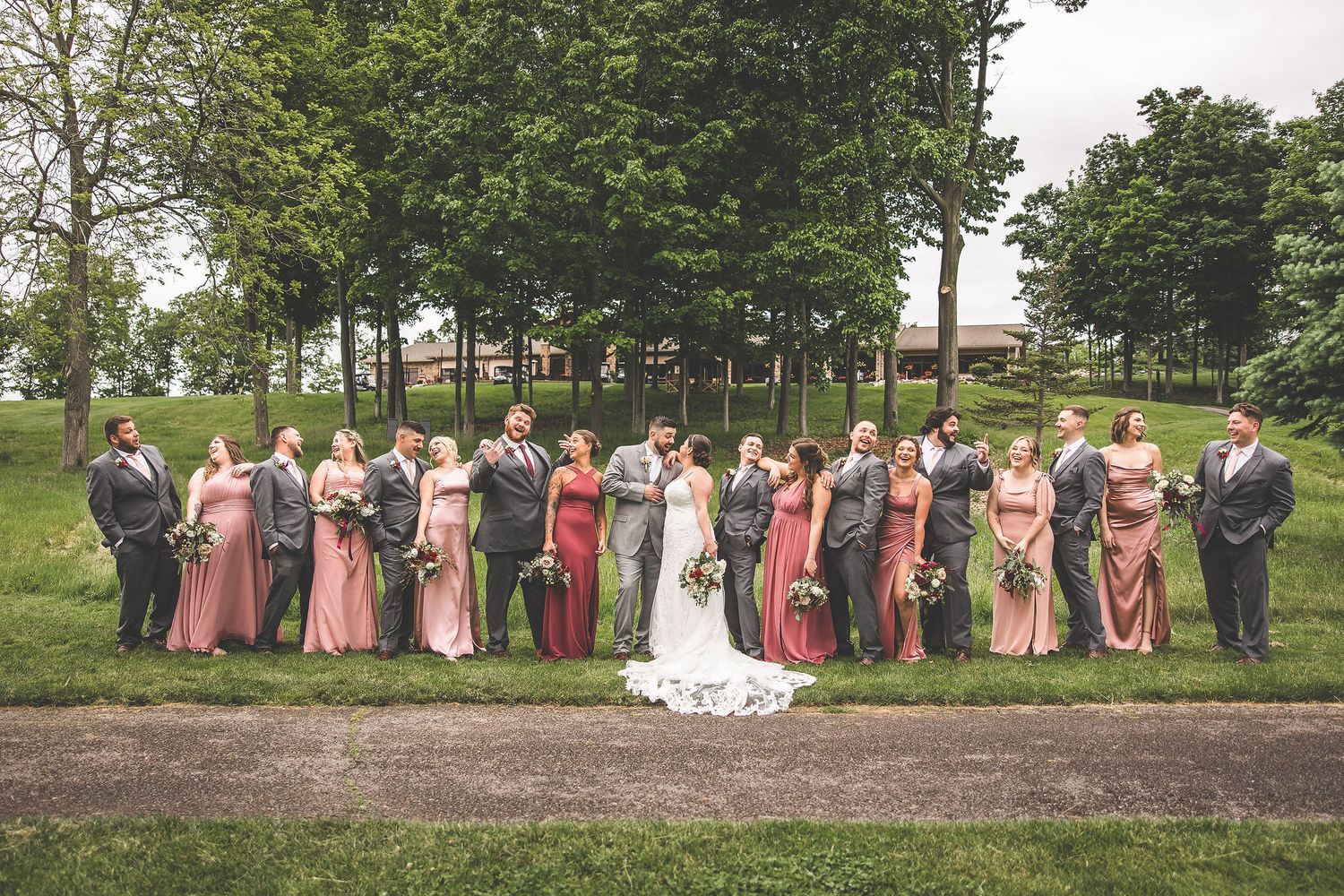 Large wedding party poses for formal photos on a rustic outdoor path.