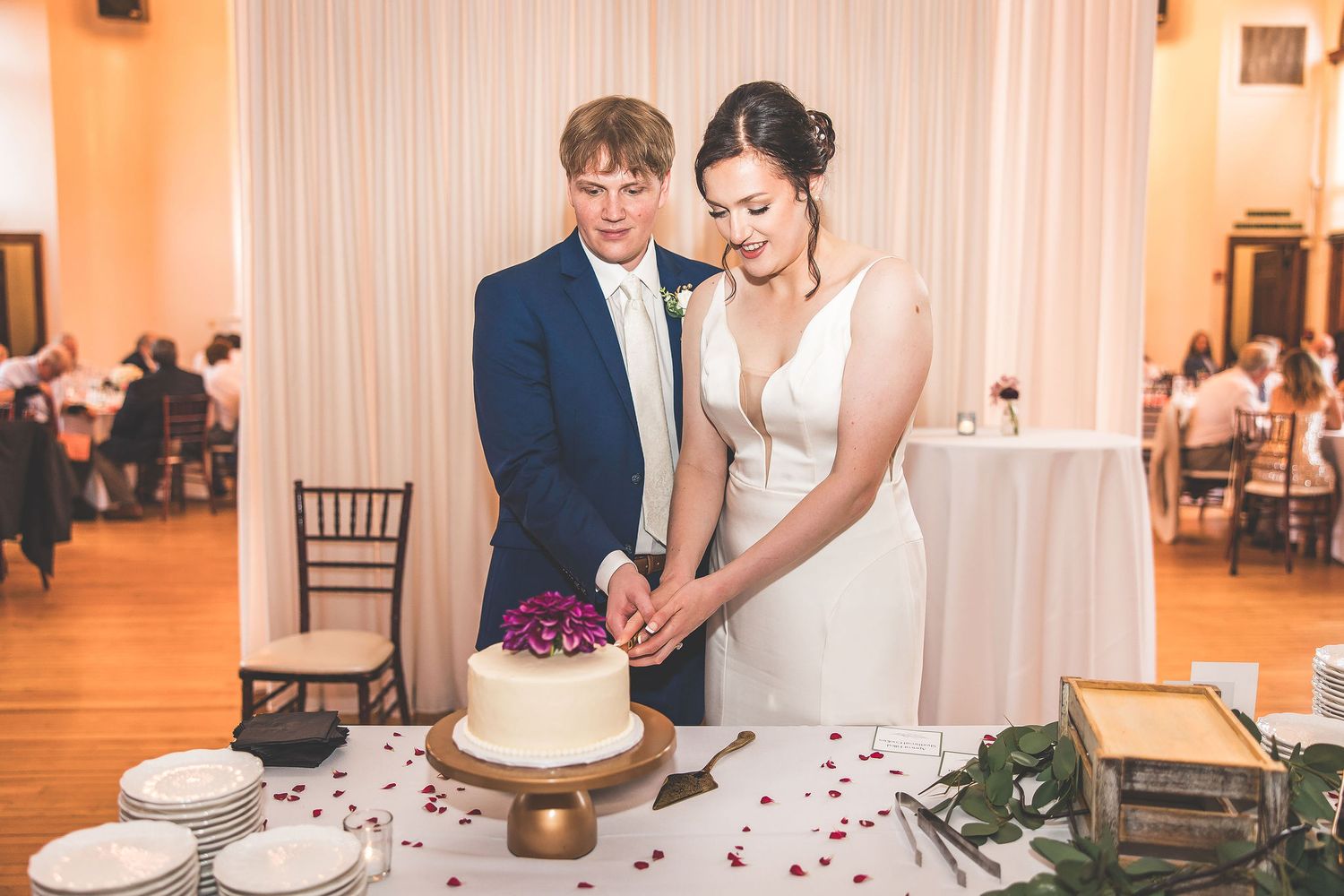Couple cuts their wedding cake together at elegant reception with white drapes.