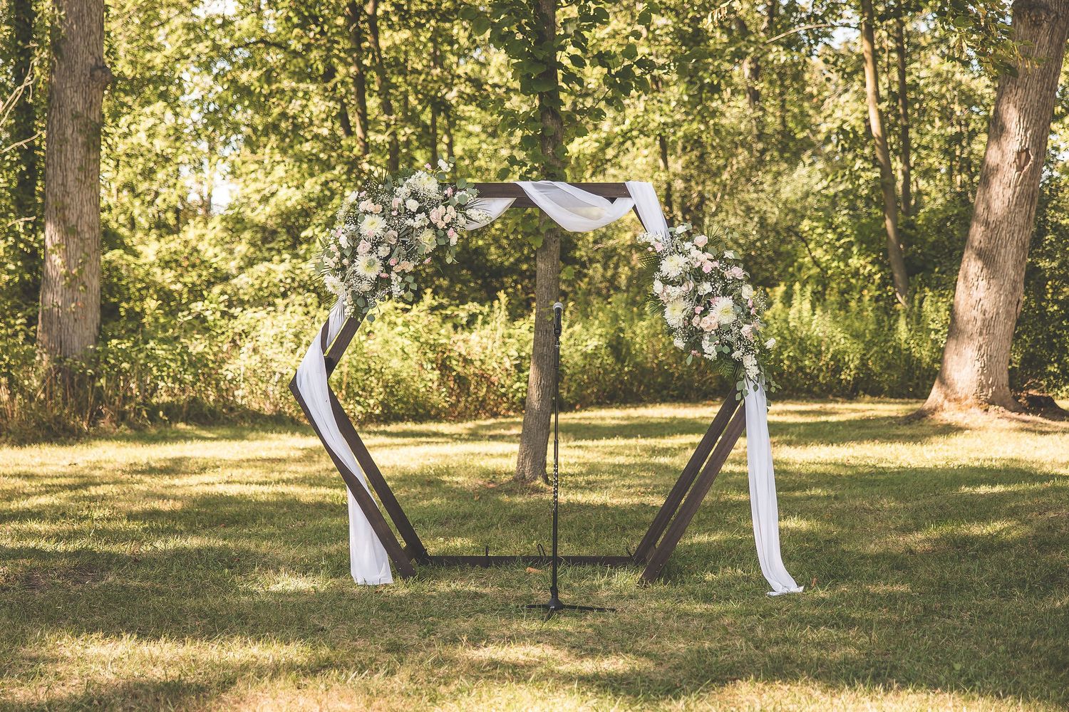 A rustic outdoor wedding ceremony setup with white chairs arranged on a grassy lawn surrounded by trees.