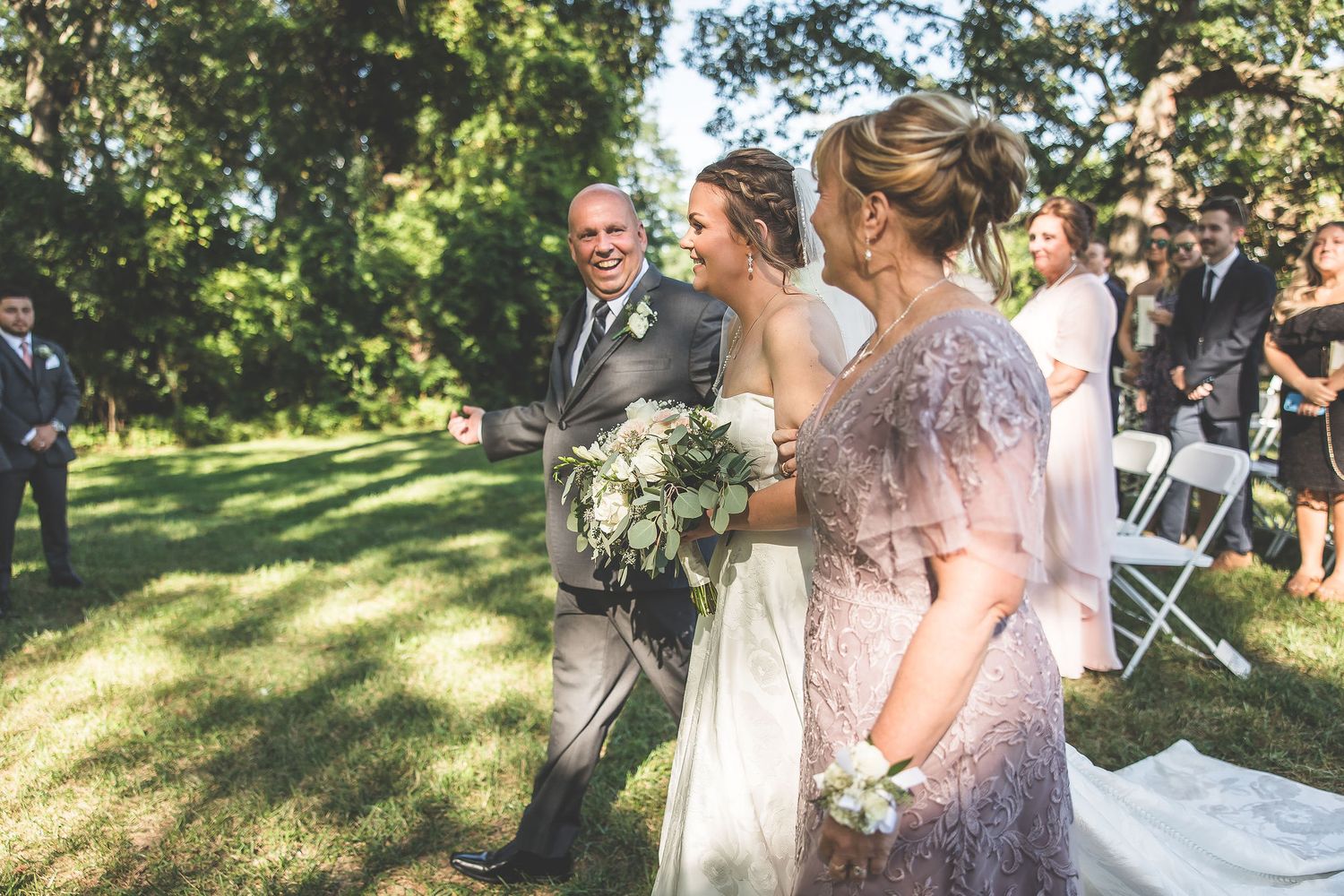 Wedding party members walking and laughing together on grassy lawn near wooden barn.