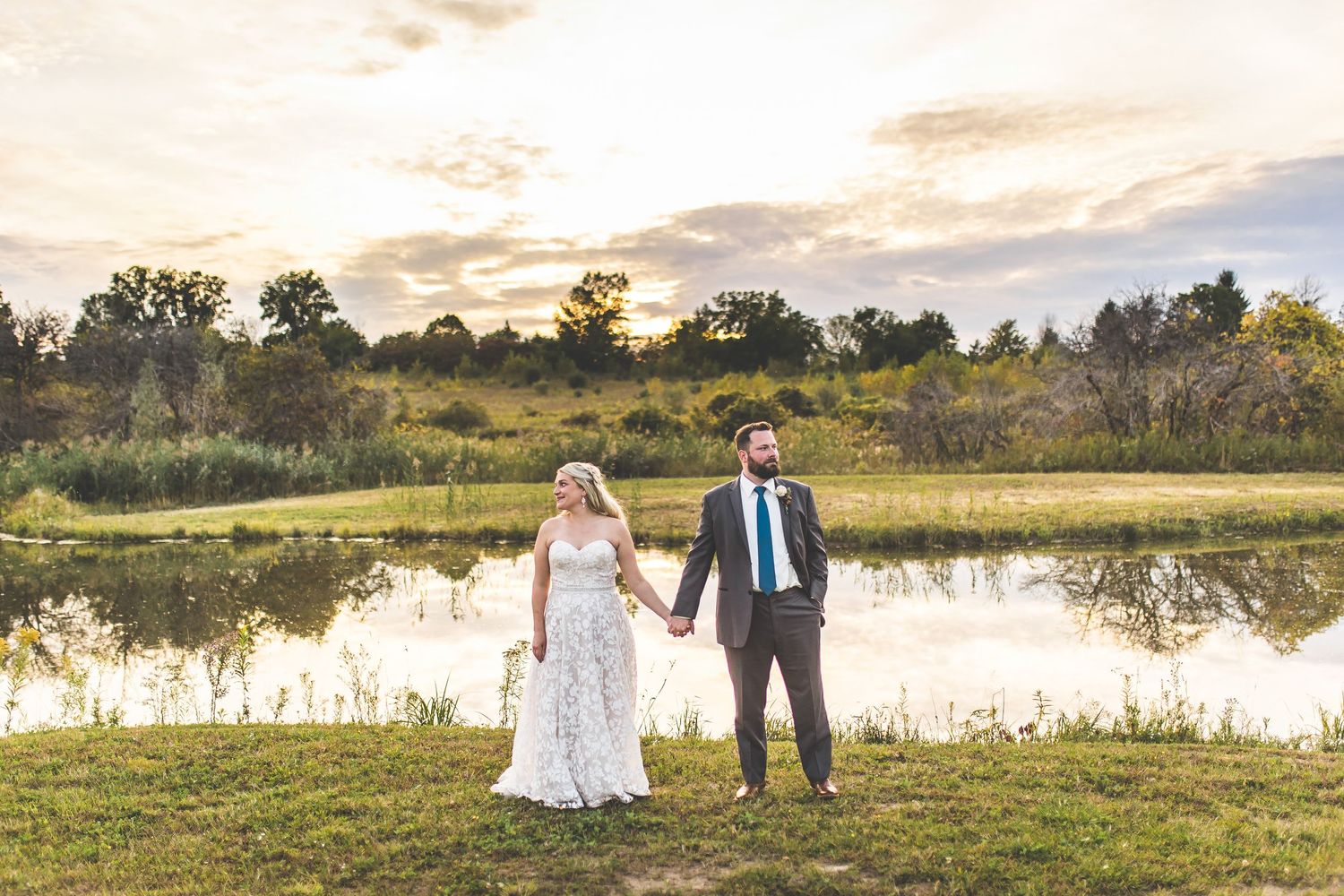 Wedding couple explores a serene lakeside setting during sunset.
