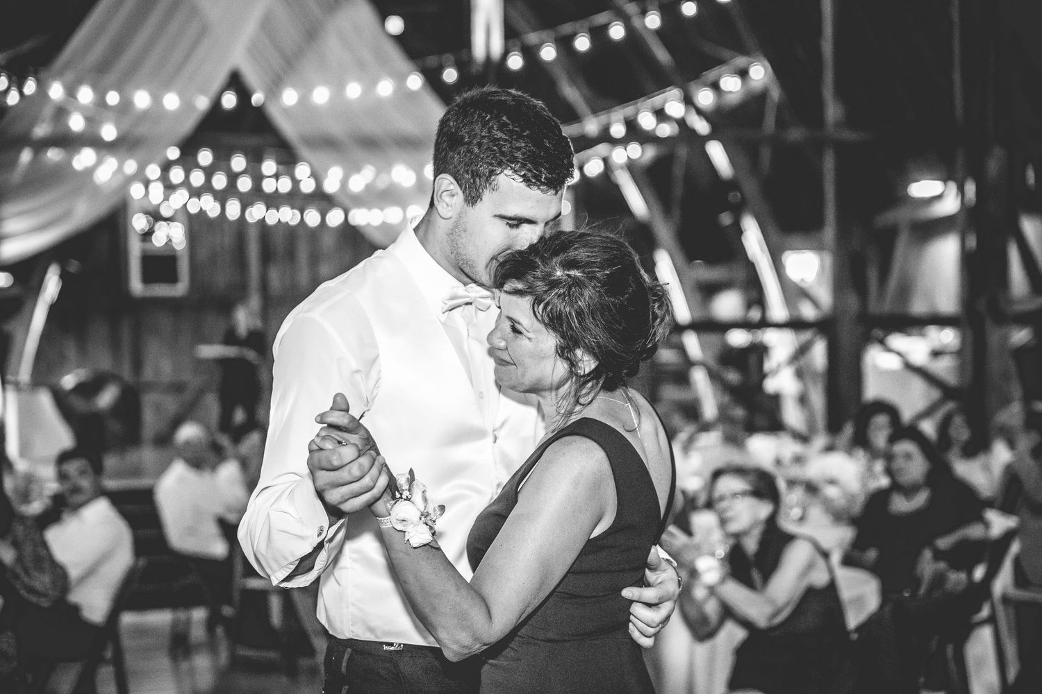 Wedding reception dance floor filled with couples dancing under twinkling lights in a barn setting.