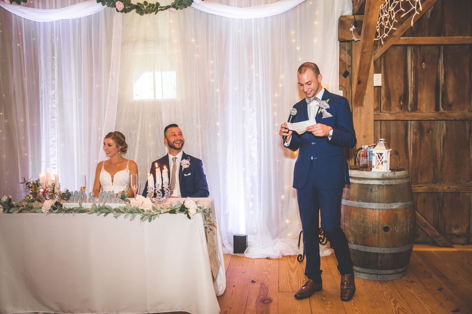 Wedding reception venue decorated with white curtains and rustic wooden barrels.