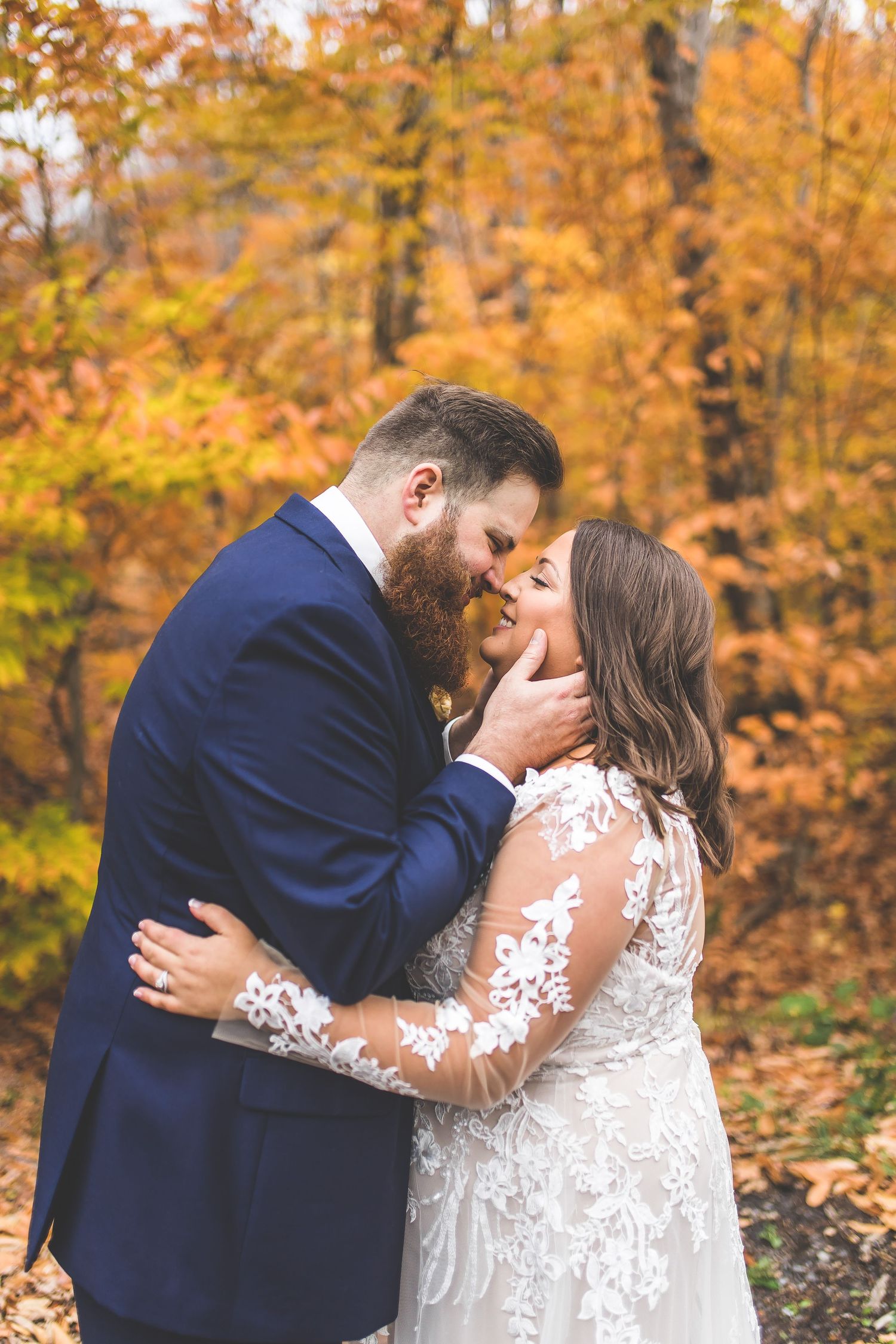A couple shares a romantic kiss in front of vibrant autumn foliage during their wedding photoshoot.