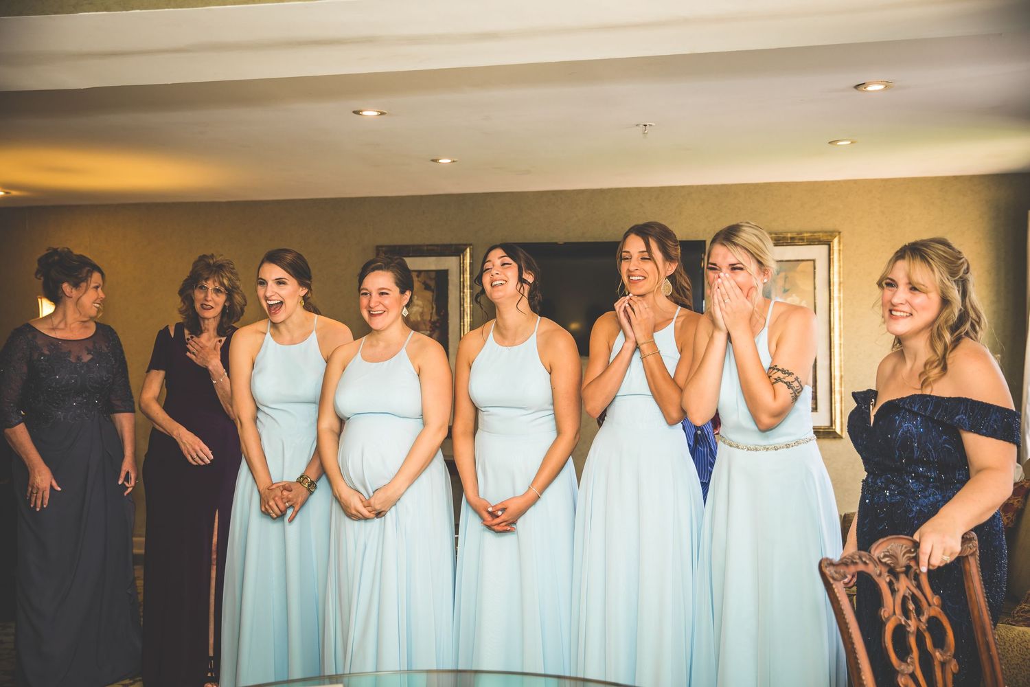 Bridesmaids in light blue dresses and one in navy stand together in a row at a wedding celebration.