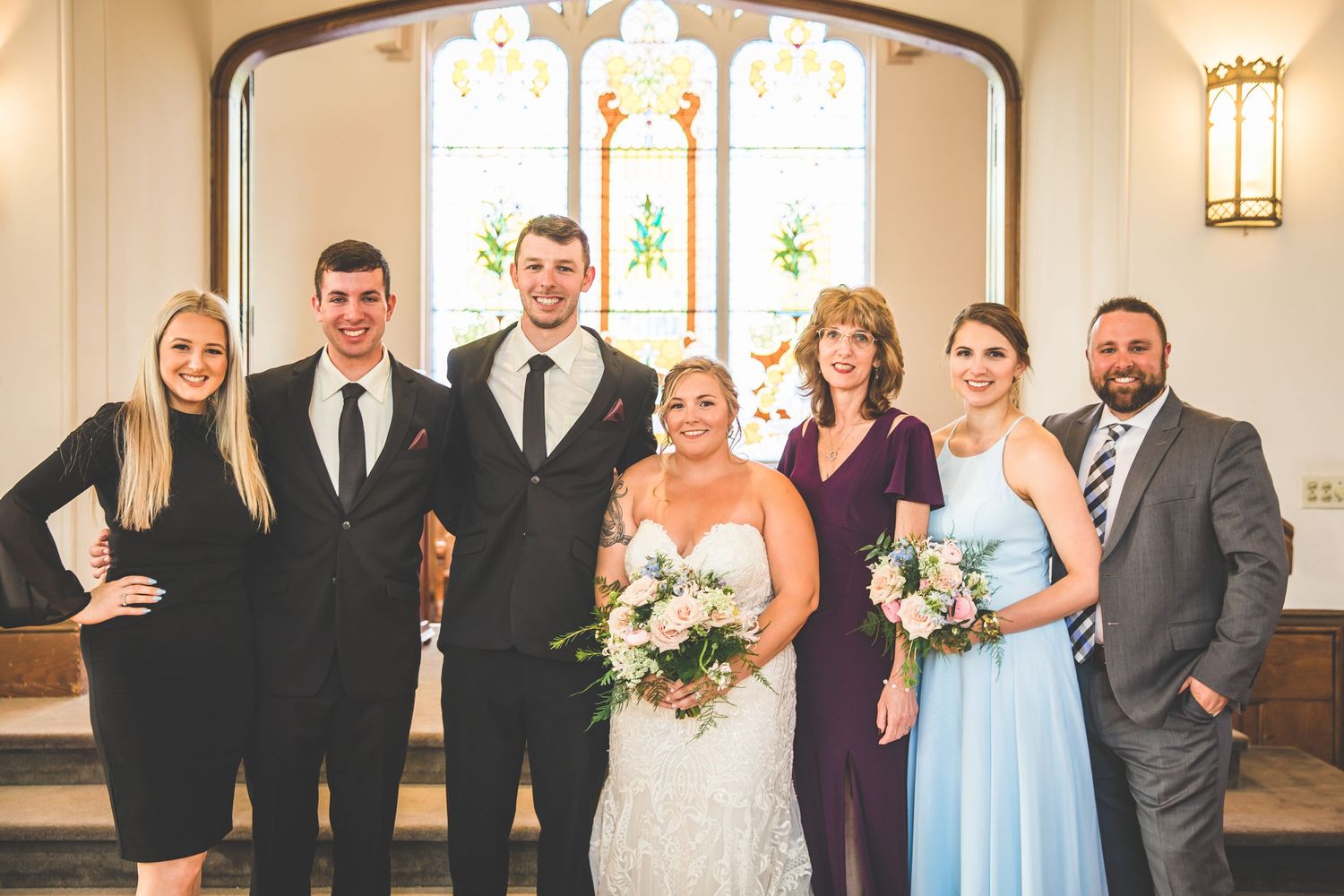 Wedding party group photo in church with bridesmaids in blue and purple dresses.