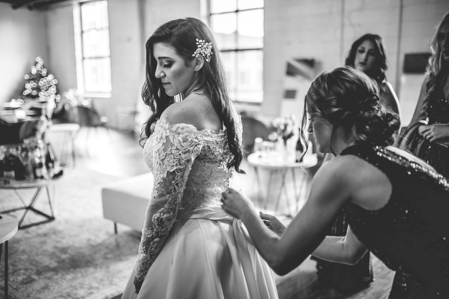 Getting ready scene with bridesmaids helping with wedding dress preparations.