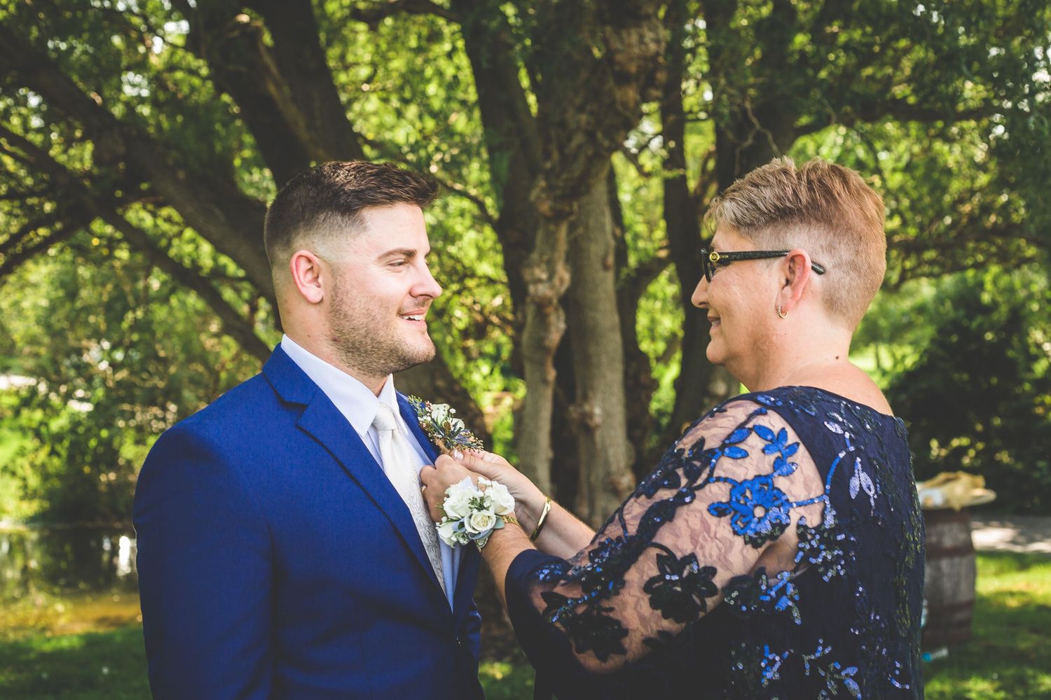 Boutonniere being pinned on groom's royal blue suit jacket outdoors.
