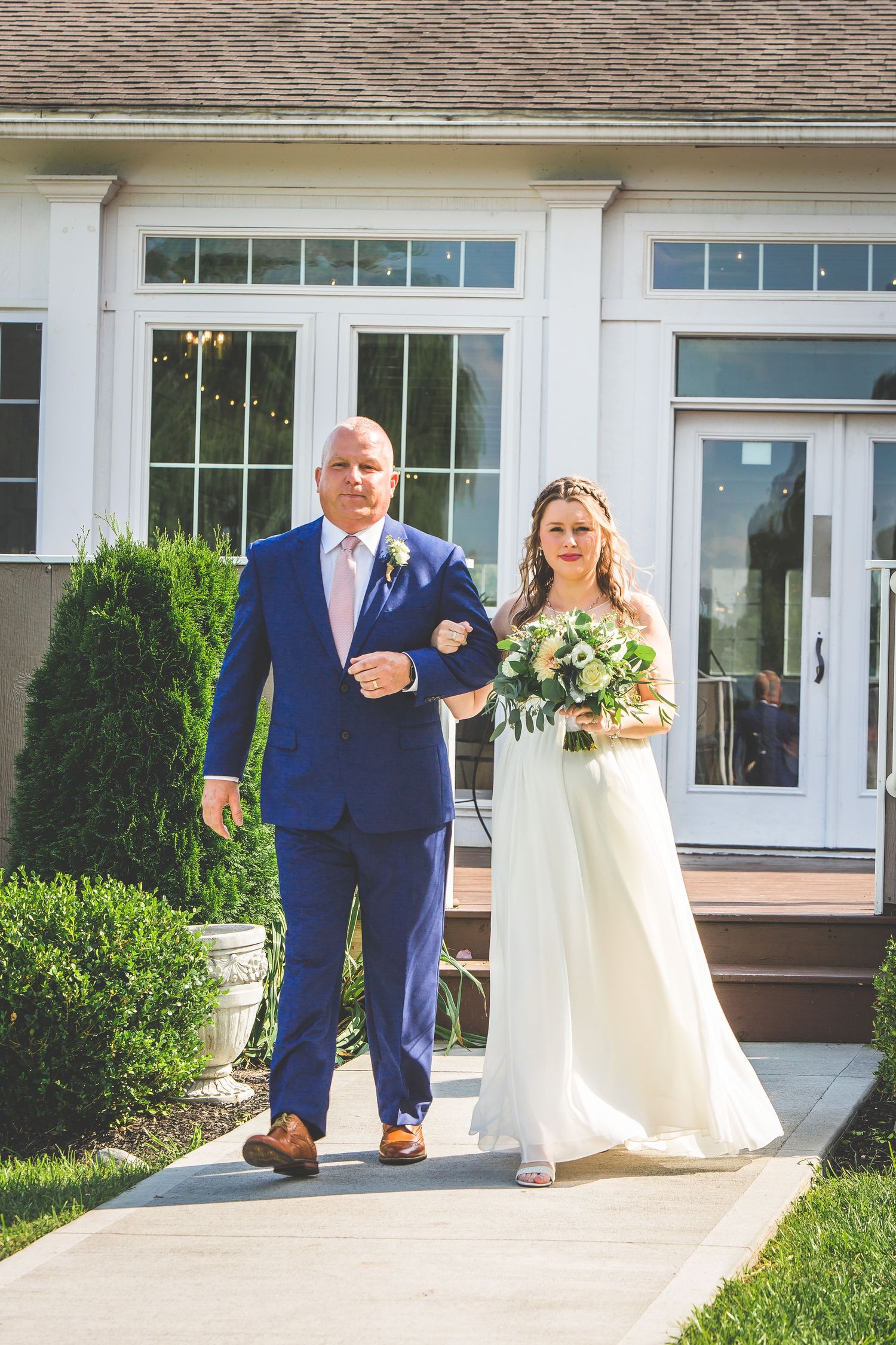 Wedding couple walking together outside venue in blue suit and white dress.