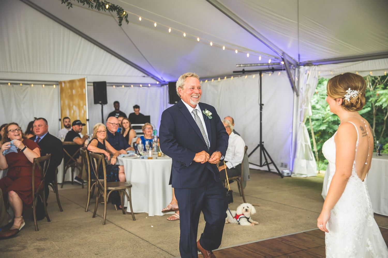 Wedding reception under white tent with string lights and decorative greenery.