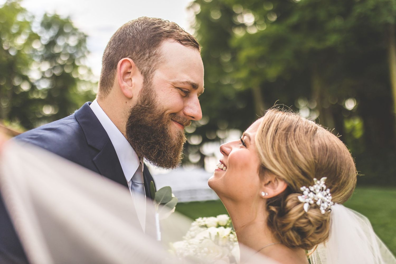 Romantic wedding couple sharing tender moments along a tree-lined path in natural lighting.