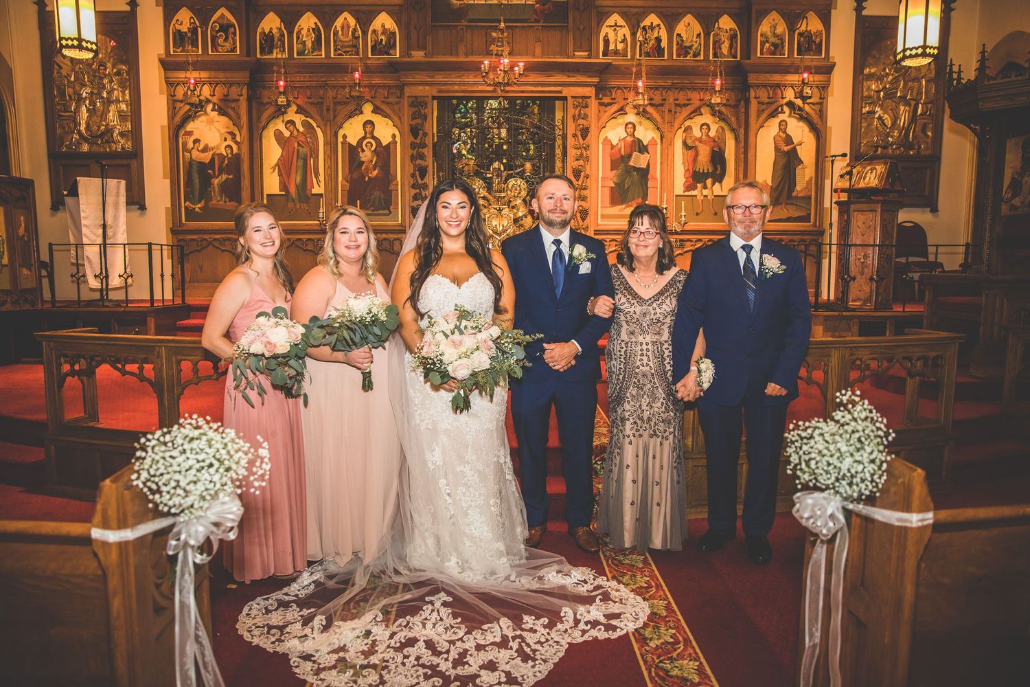 Wedding party poses together in front of church altar with ornate religious artwork and decorative flowers.
