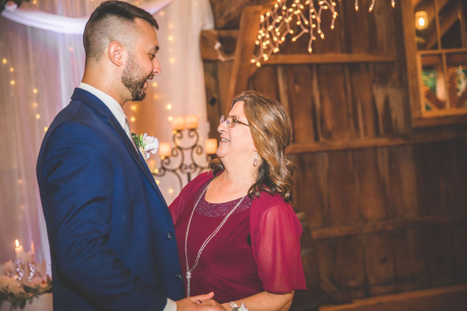 Wedding reception in a rustic barn venue with burgundy decor and string light ambiance.